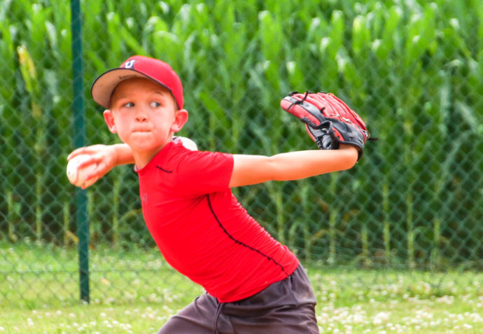 Boy in red shirt winding up to throw the baseball