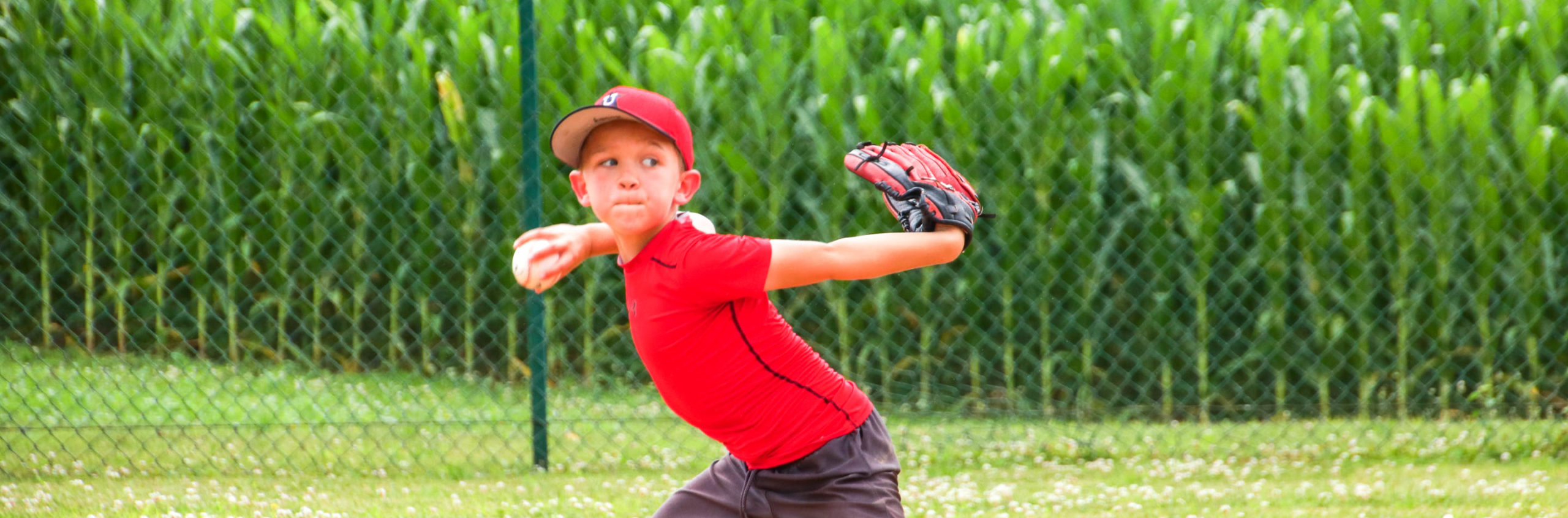 Boy in red shirt winding up to throw the baseball