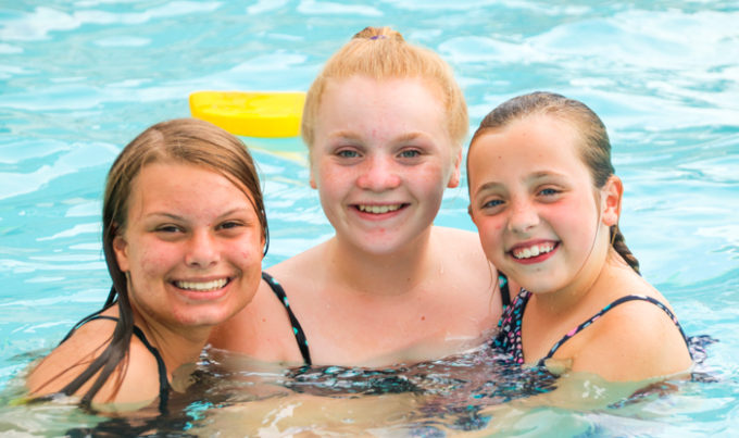 Three campers in the swimming pool smiling for a photo