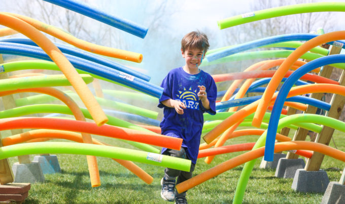 Young boy camper running through the color run course through a bunch of pool noodles