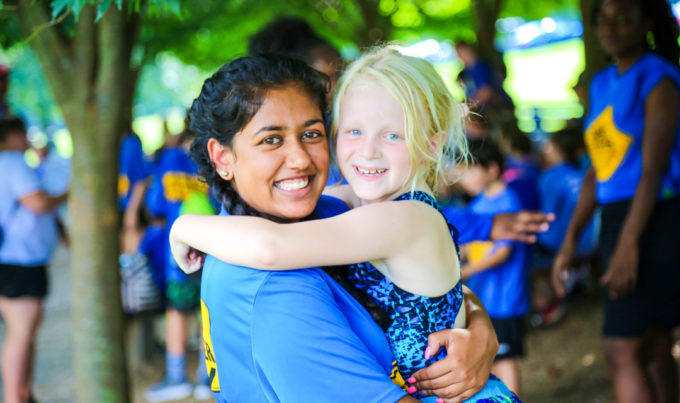 Counselor carrying a young girl camper with her arms around the counselors neck