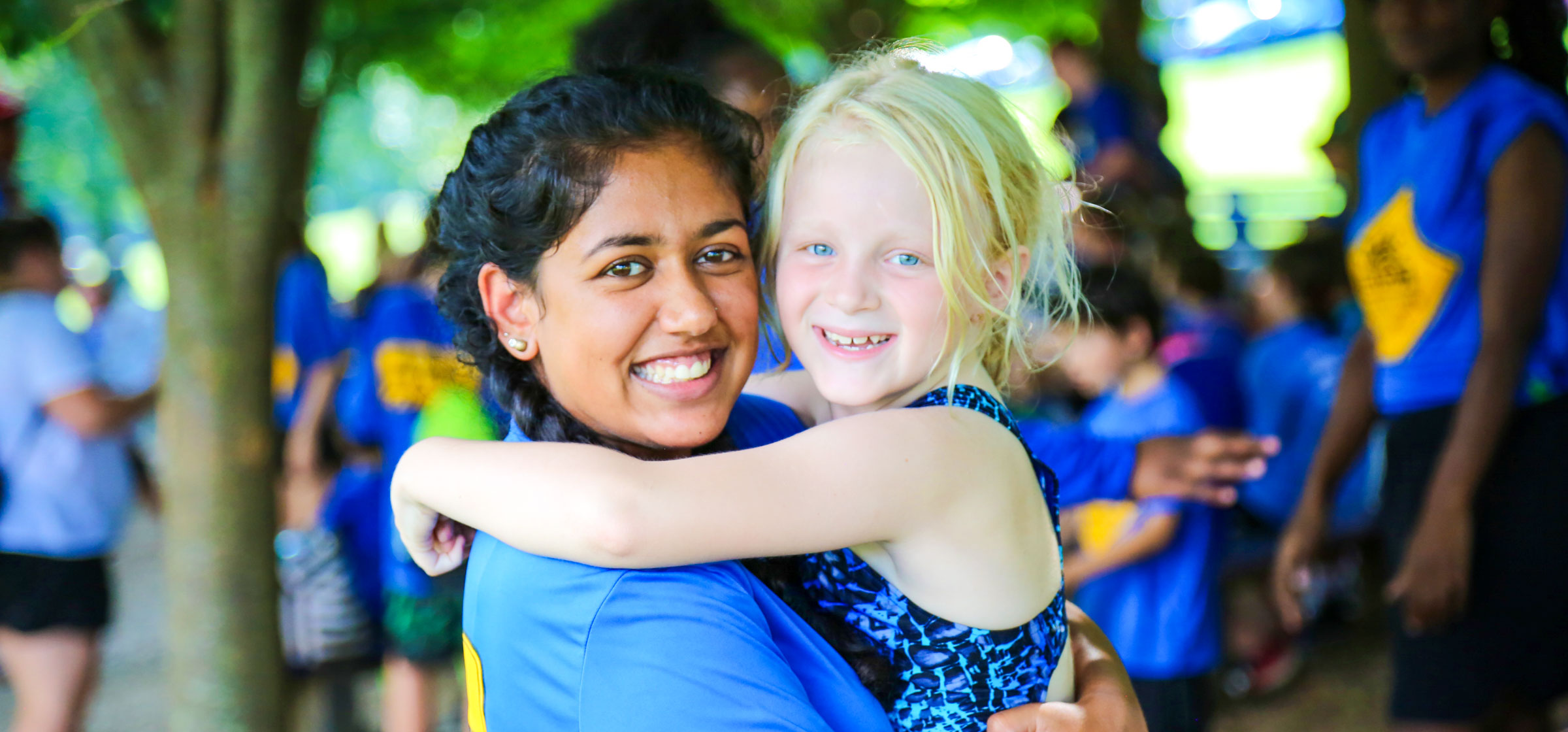 Counselor carrying a young girl camper with her arms around the counselors neck