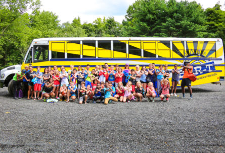 A large group of campers squatting and standing in front of a Bar-T bus taking a group photo