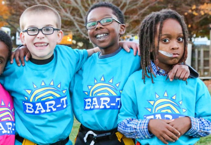 Four kids with flag football flags on and light blue shirts arms around each other for a photo