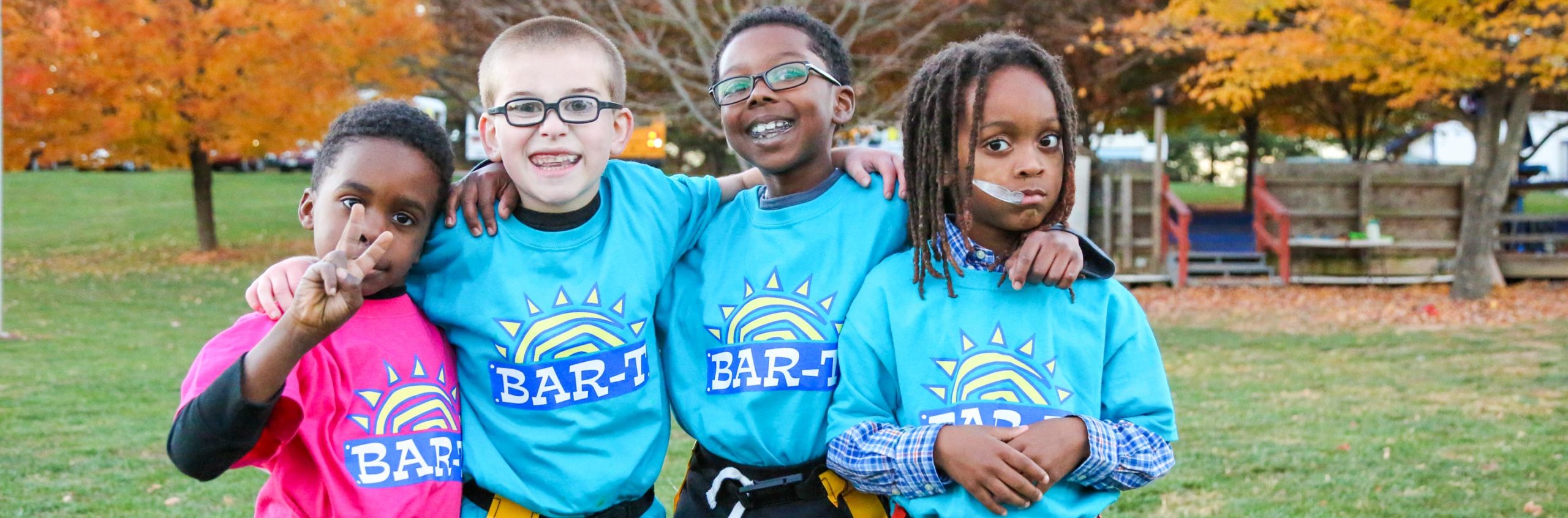 Four kids with flag football flags on and light blue shirts arms around each other for a photo