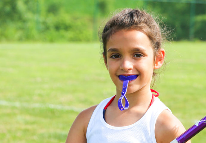 Girl with mouth guard holding a lacrosse stick on the field