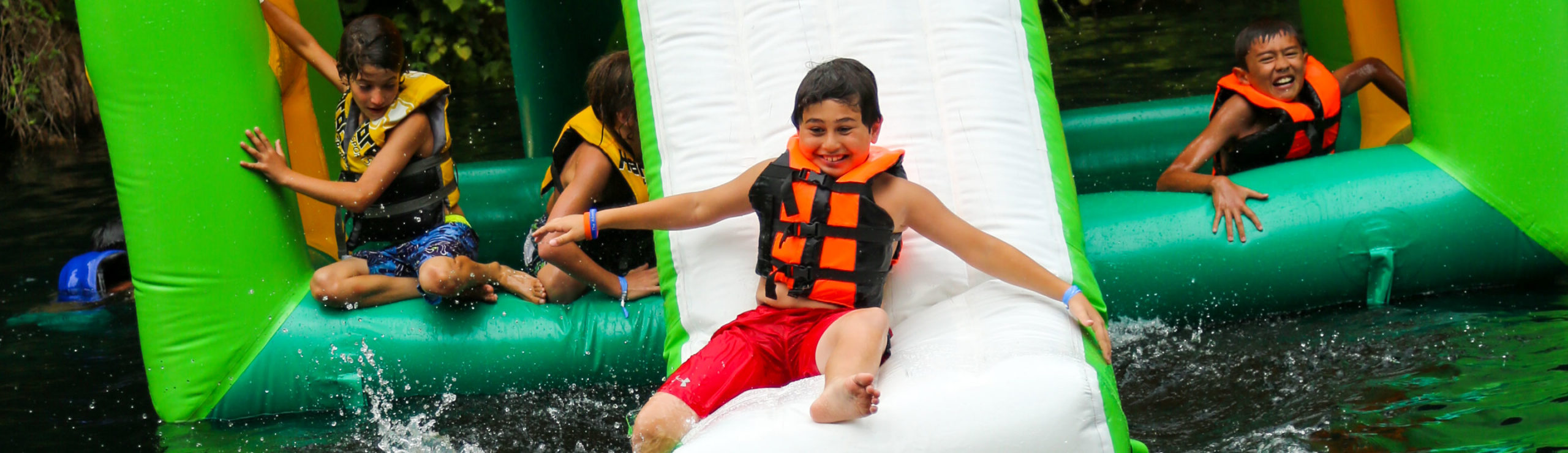 Camper sliding down a large inflatable slide into the lake