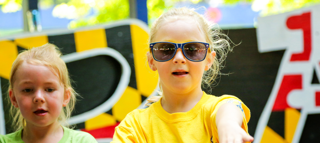 Girl camper in sunglasses and a yellow camp shirt dancing on stage